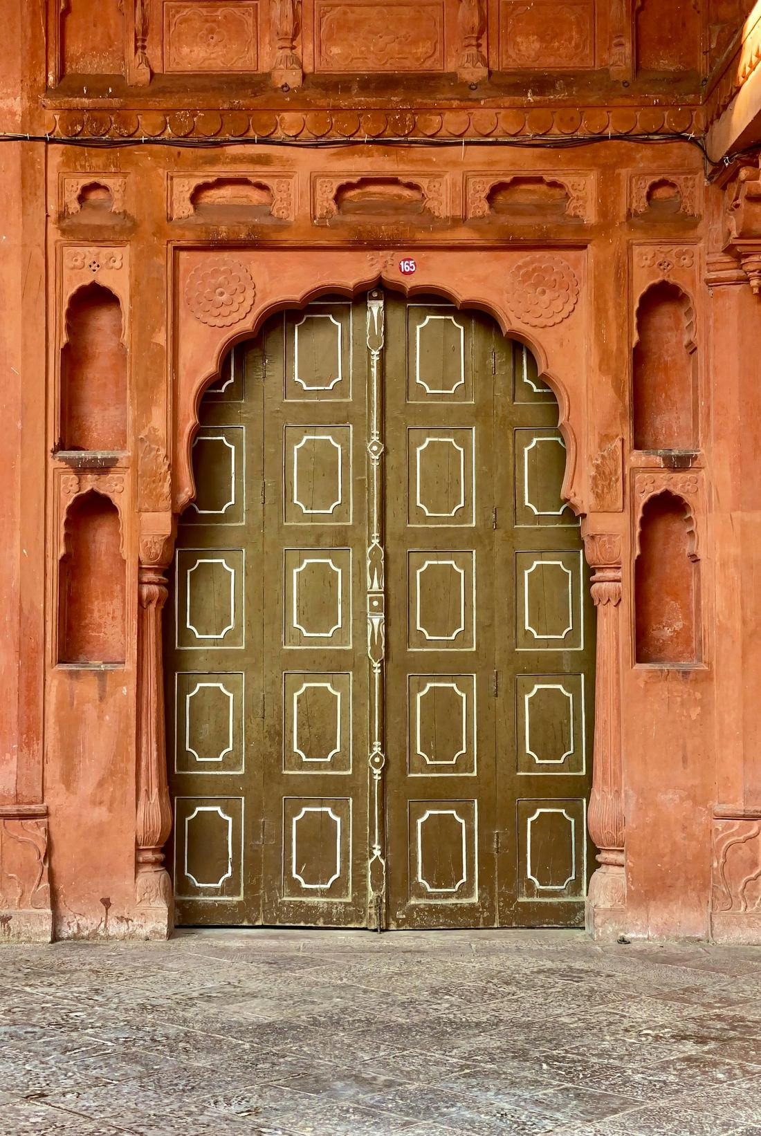 A carved red sandstone doorway with painted wooden doors.